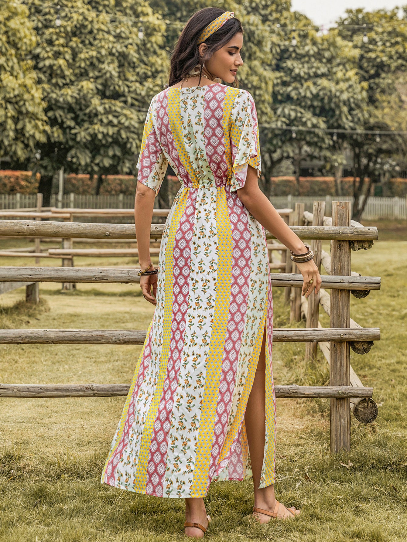 Woman in a patterned dress standing in a grassy field with wooden fences.