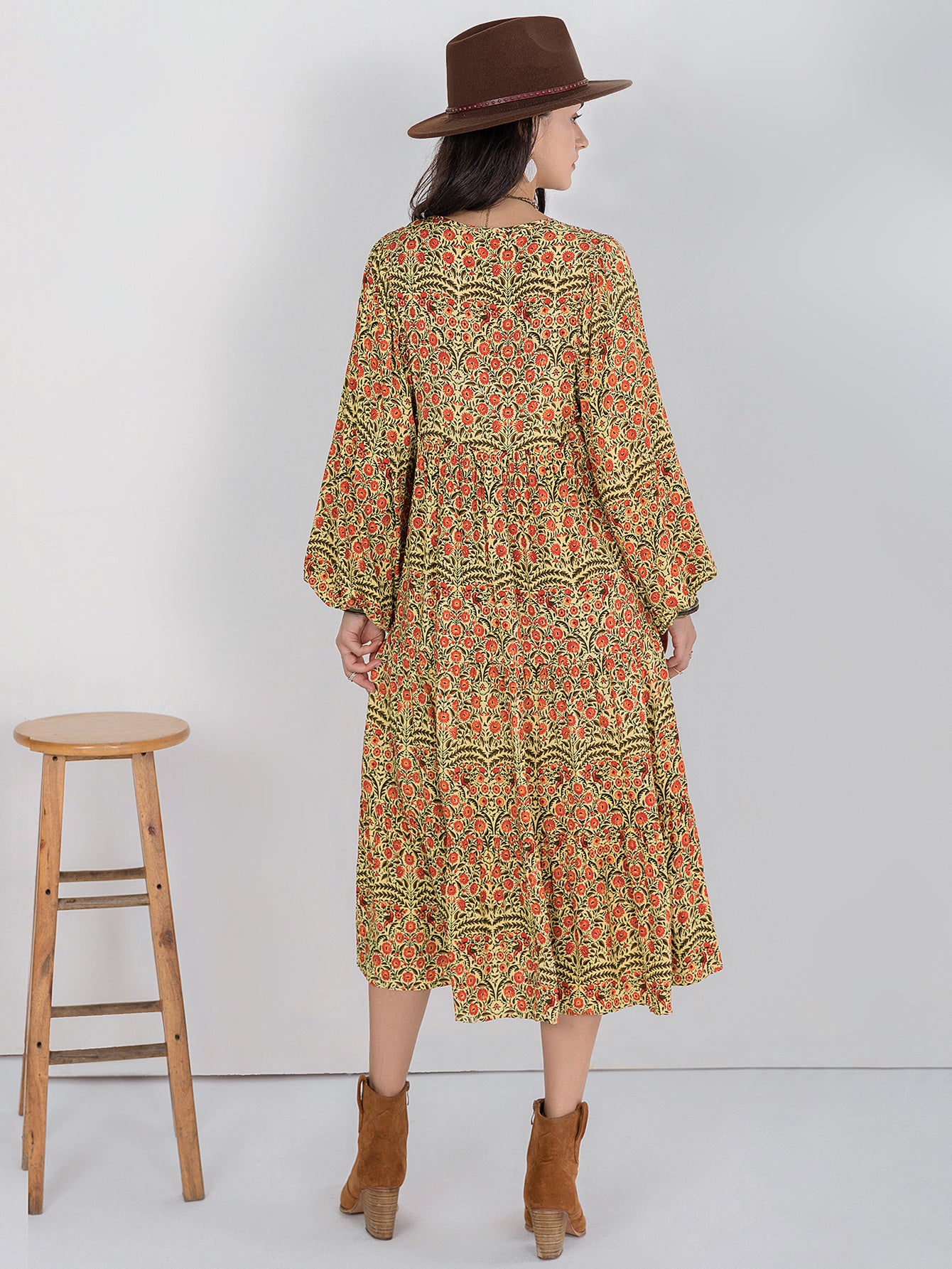 Woman wearing a patterned dress and brown hat, standing next to a wooden stool on a white background
