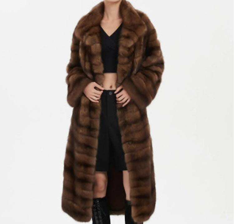 Person wearing a long brown fur coat on a white background