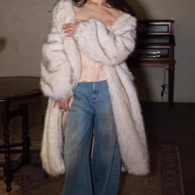 Person wearing a long white fur coat and blue jeans indoors.