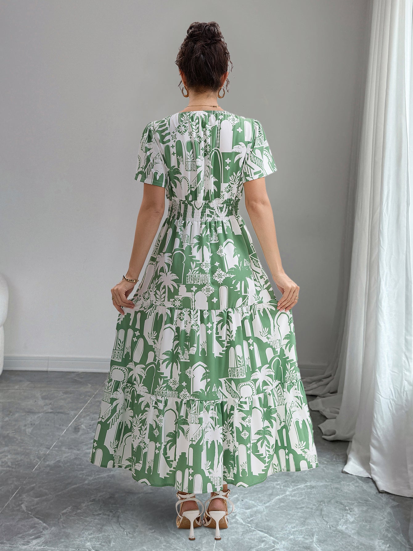 Woman wearing a green and white patterned dress in a room with gray flooring and white curtains.