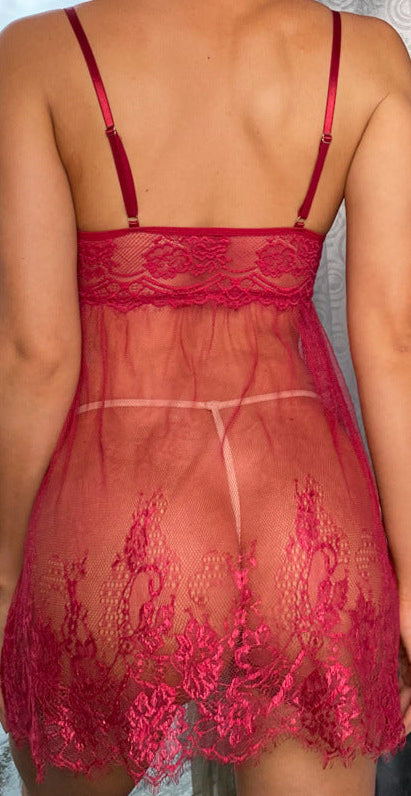 Woman wearing a red lace nightgown standing by a window with a view of buildings.