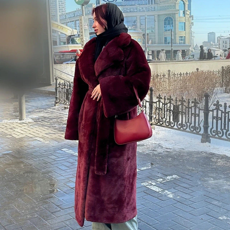 Person wearing a long burgundy coat and carrying a matching handbag on a city street.