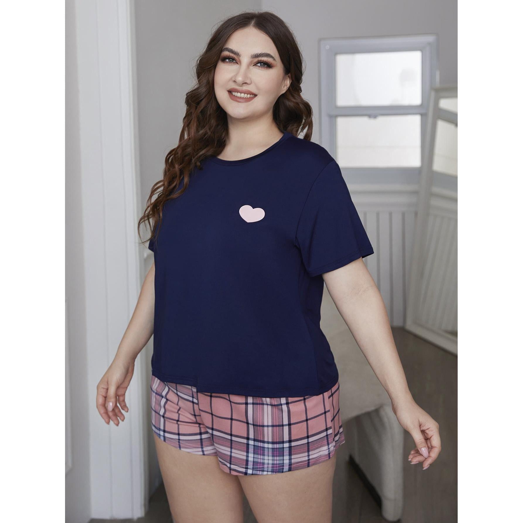 Woman wearing a navy blue t-shirt with a pink heart and plaid shorts indoors.