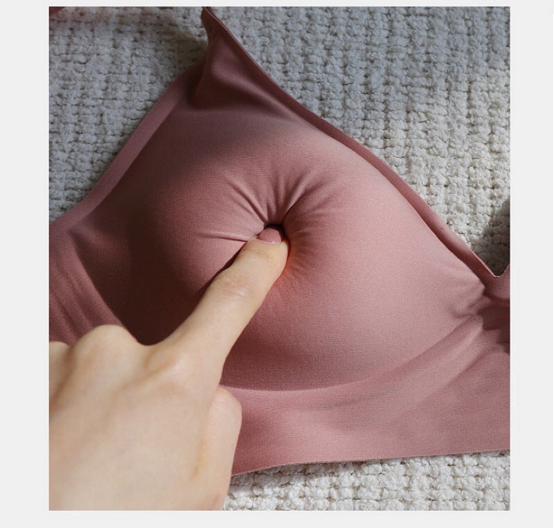 Pink travel neck pillow with a hand pressing on it against a textured carpet background