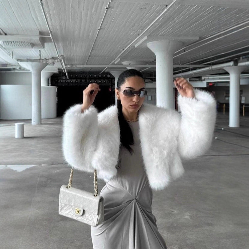 Woman in a white fur coat and silver dress holding a handbag in an indoor setting.