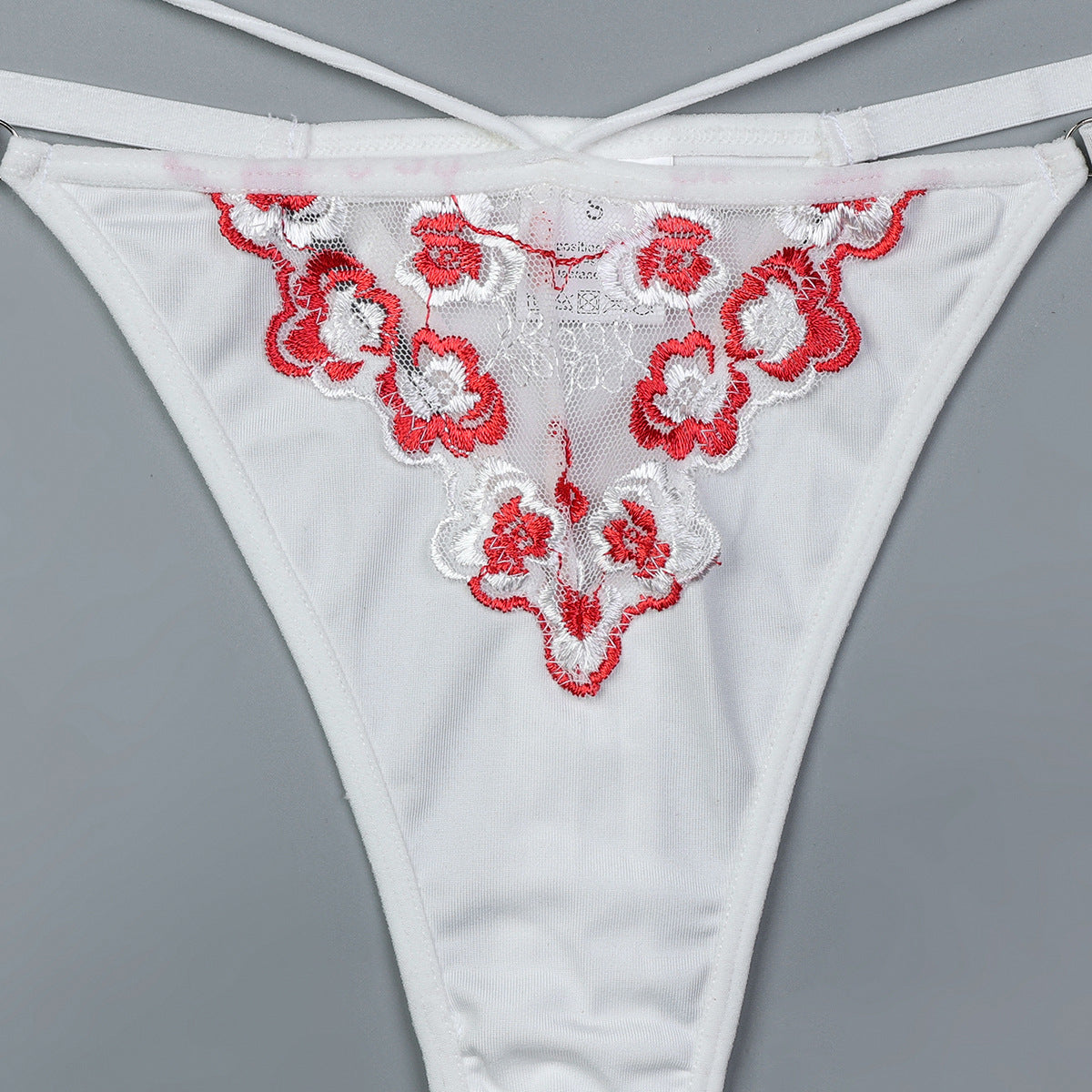 White lace thong with red floral embroidery on a gray background