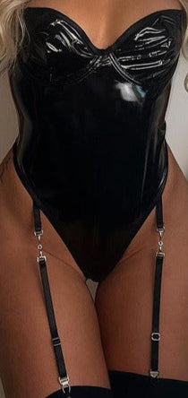 Woman wearing a black vinyl bodysuit with garters against a neutral background