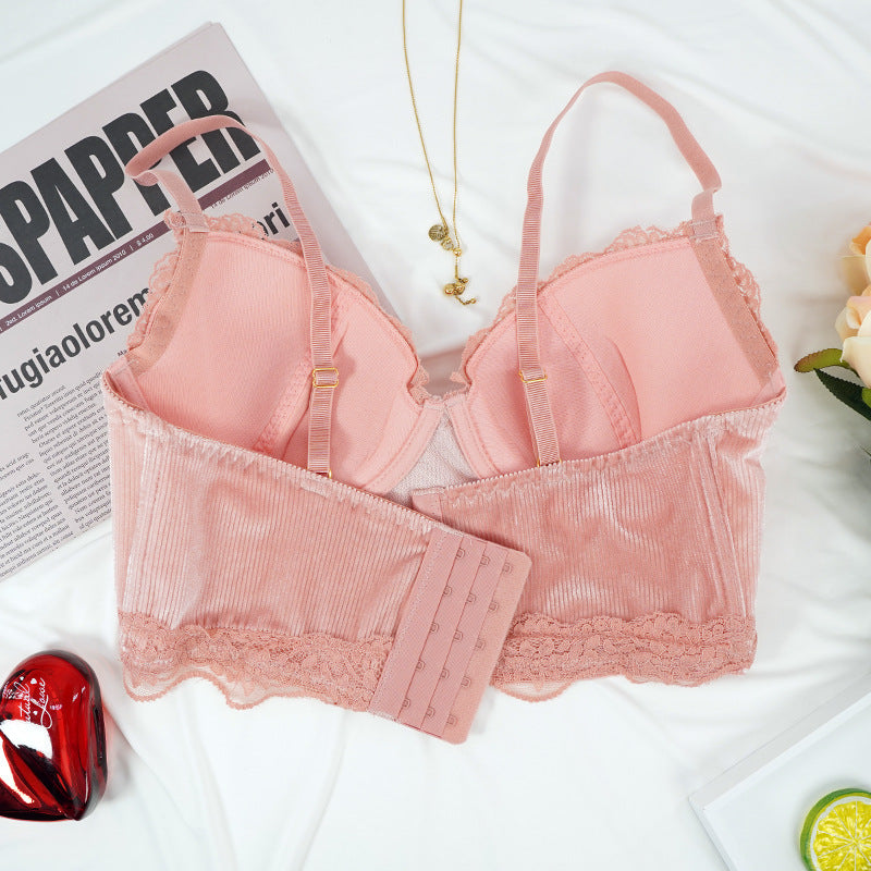 Pink bra with lace details on a white surface with a newspaper and decorative items.