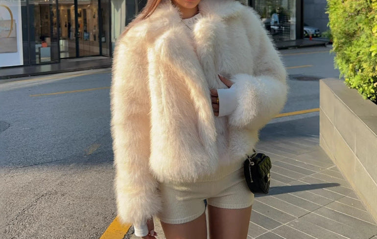 Woman wearing a white fur coat and shorts standing on a sidewalk.