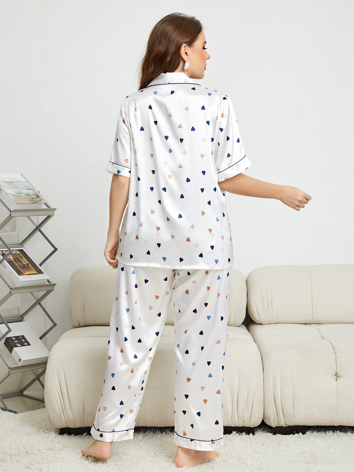 Woman wearing a white pajama set with colorful heart patterns in a living room.