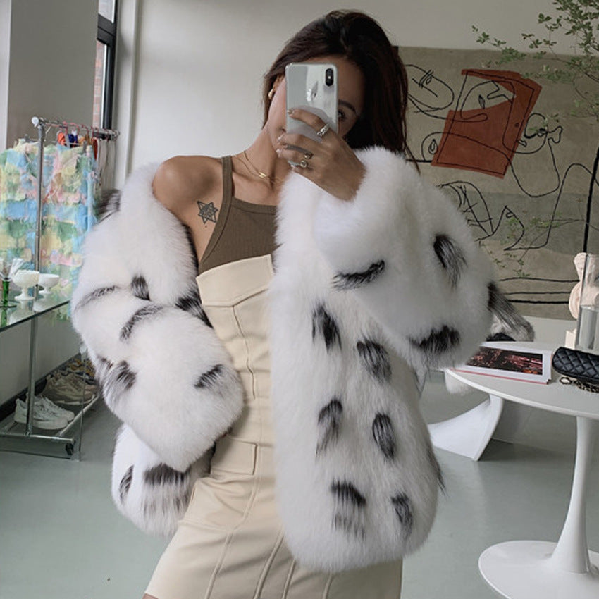 Person wearing a white fur coat with black spots, taking a mirror selfie in a modern living room.