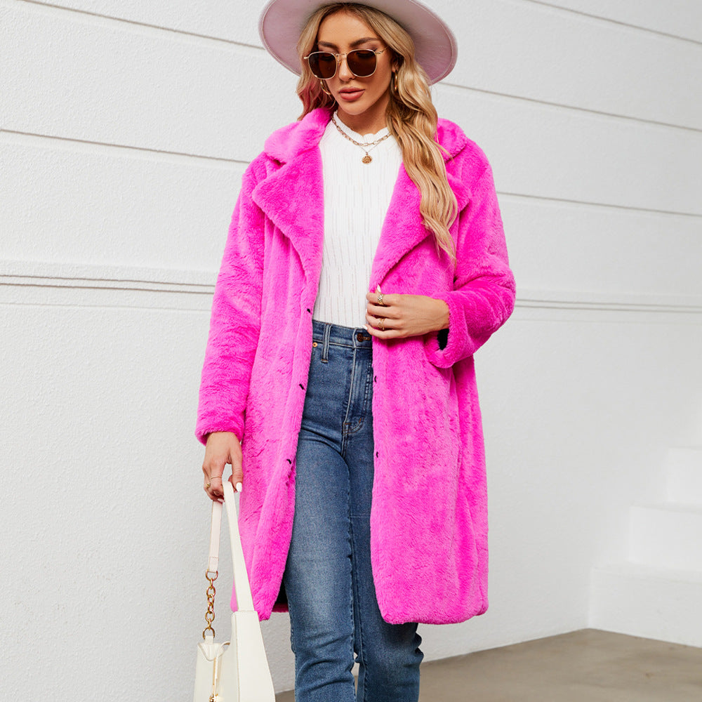 Woman wearing a bright pink coat, white top, blue jeans, and a white hat against a light background.