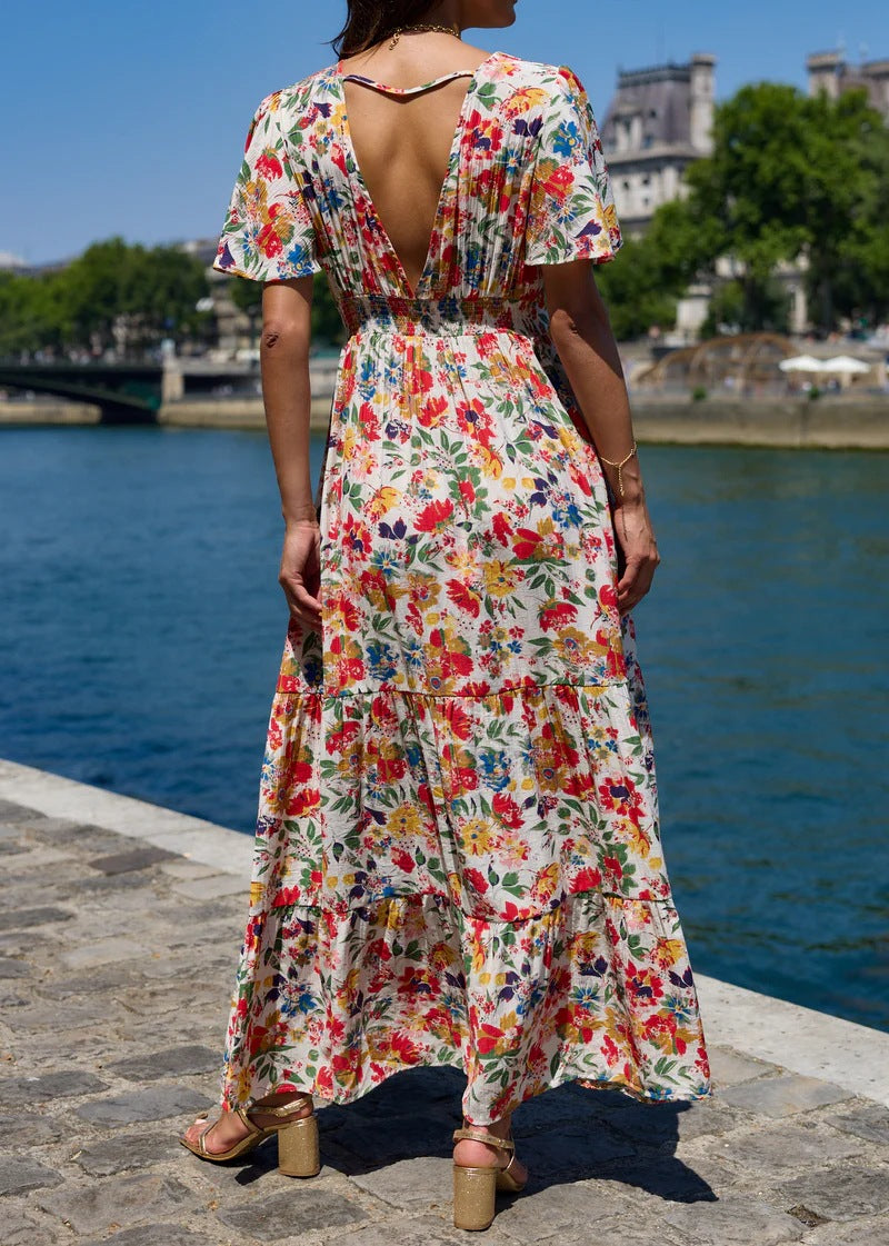 Woman in a colorful floral dress standing by a waterfront with a cityscape in the background