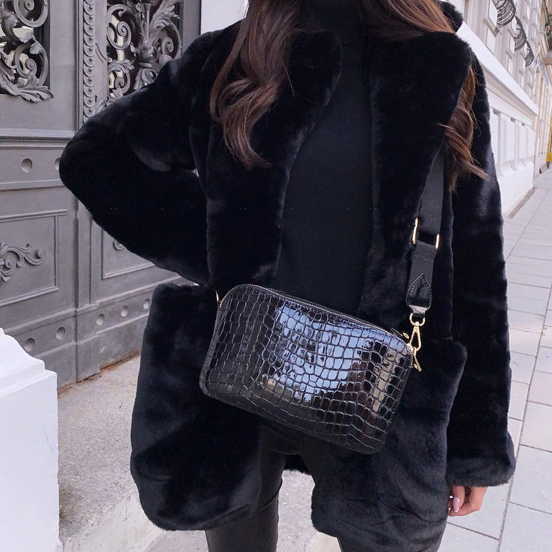 Person wearing a black fur coat holding a black crocodile-patterned handbag.