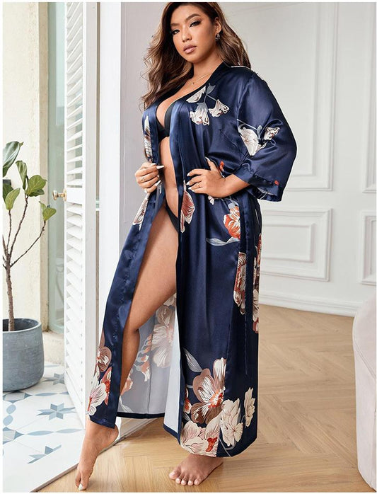 Woman wearing a navy floral satin robe in a room with white walls and a plant.