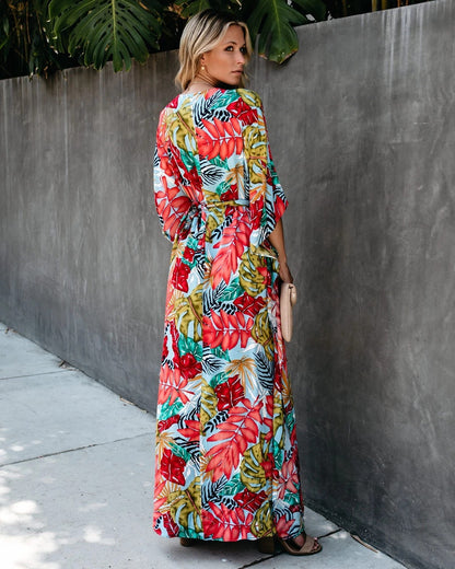 Woman wearing a colorful floral dress against a gray wall.