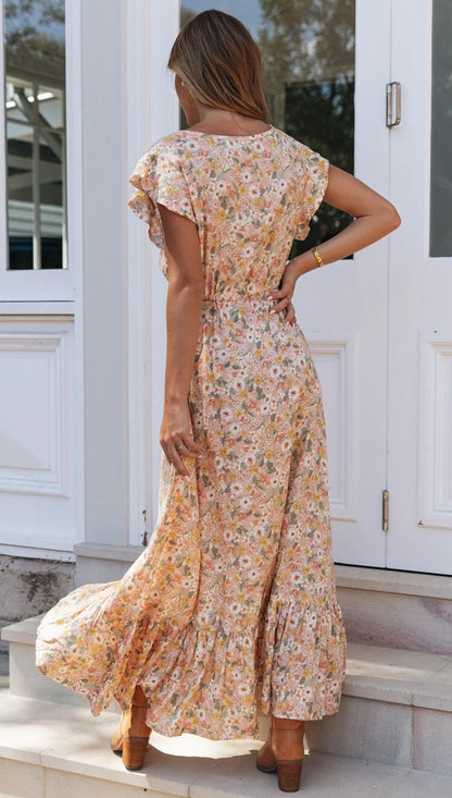 Woman in a floral dress standing on steps outside a white building.