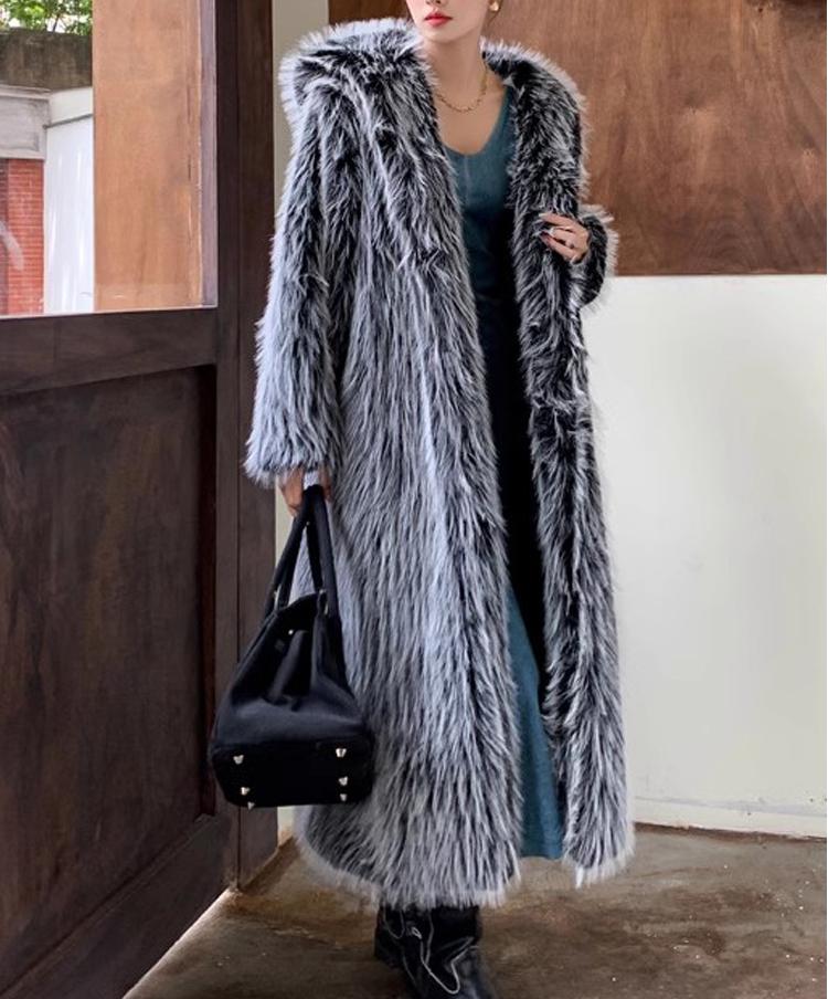 Person wearing a long, fluffy gray coat holding a black handbag indoors.