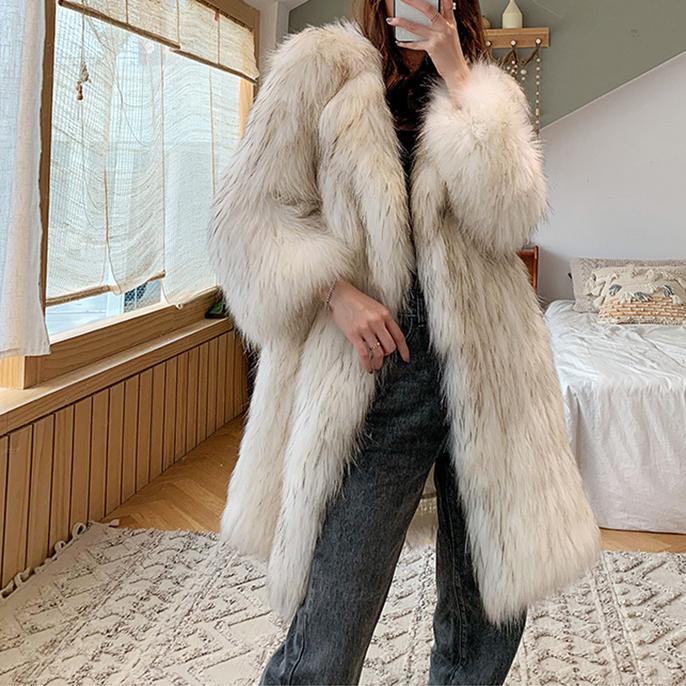 Person wearing a long white fur coat in a bedroom setting.