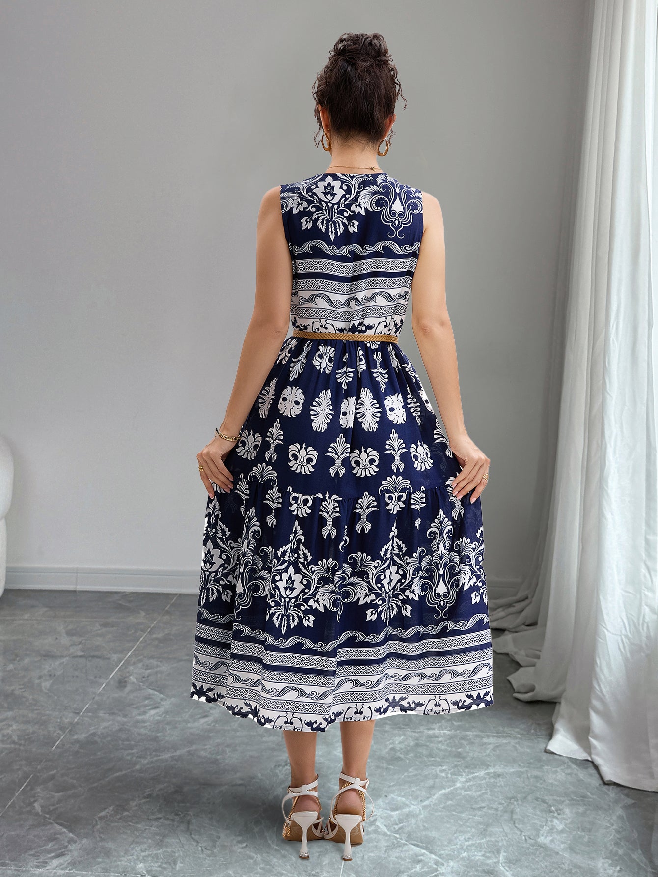Woman wearing a navy blue and white patterned dress in a room with gray walls and white curtains.