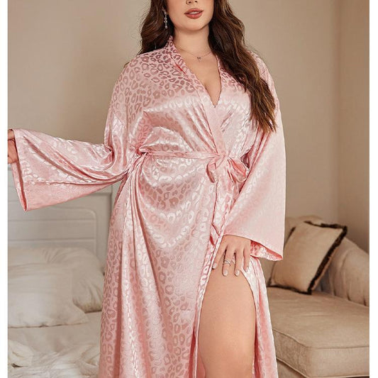 Woman wearing a pink satin robe with a leopard print pattern in a bedroom setting.