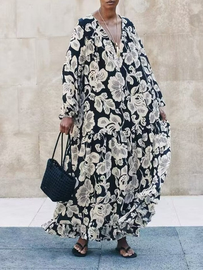 Person wearing a long black floral dress against a light stone wall.