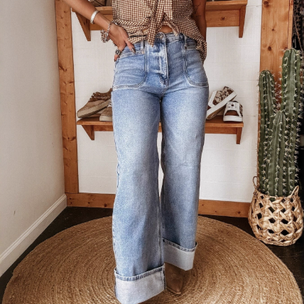 Person wearing blue jeans standing in a room with wooden shelves and a cactus plant. Women washed out mid waist straight jeans with elastic waistband