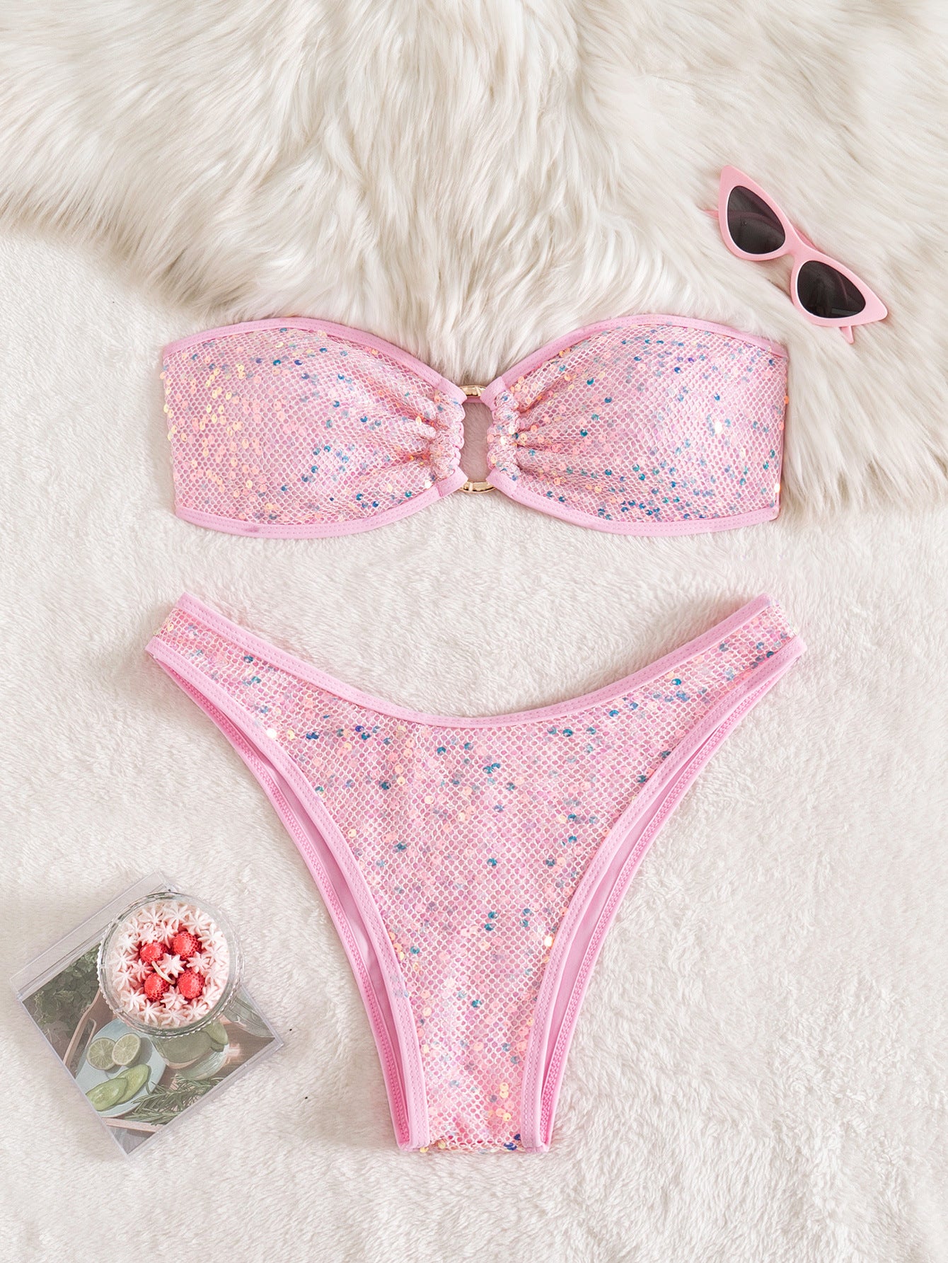 Pink bikini set with sunglasses and a magazine on a fluffy white surface