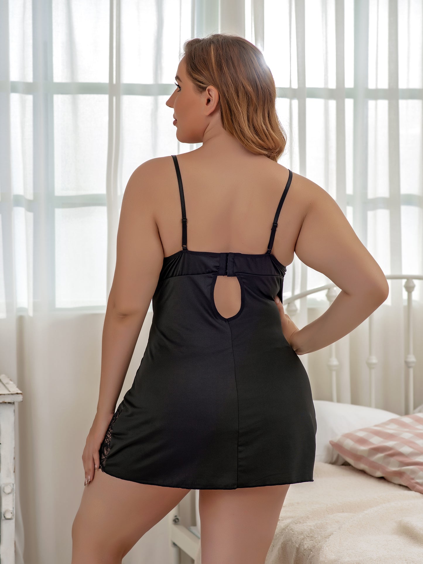 Woman wearing a black nightgown with cut-out design in a bedroom setting.