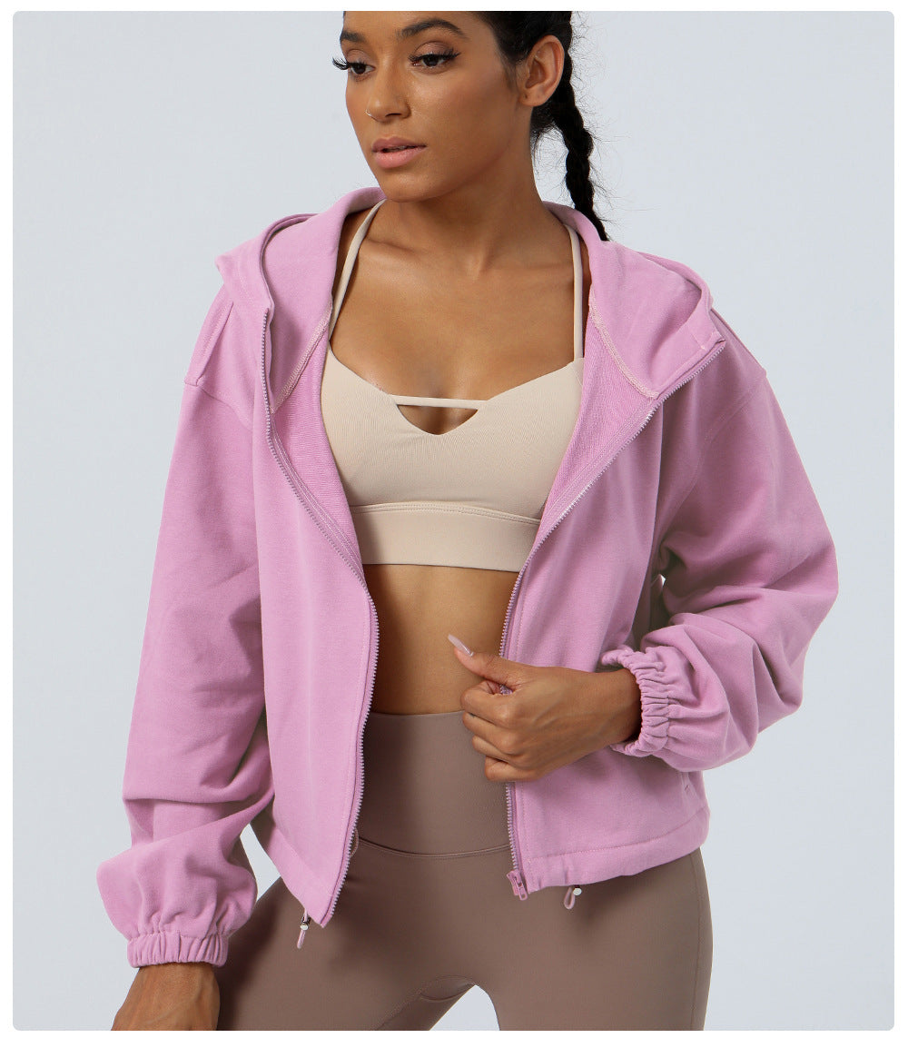 Woman wearing a pink jacket, beige sports bra, and brown leggings on a light gray background