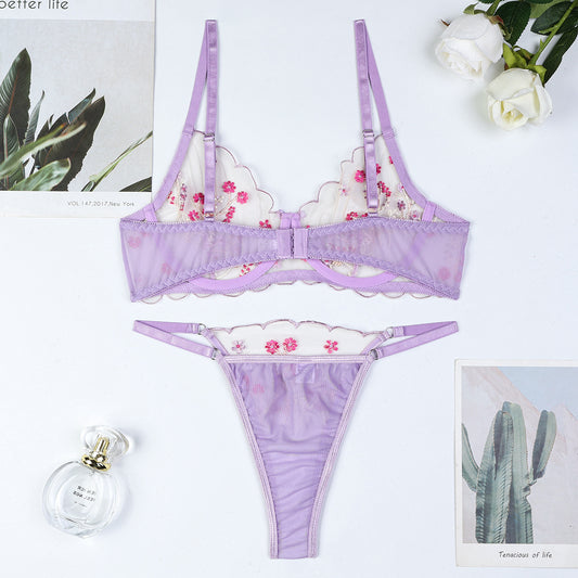 Lavender lingerie set with floral design on a white background, accompanied by a perfume bottle and plants.