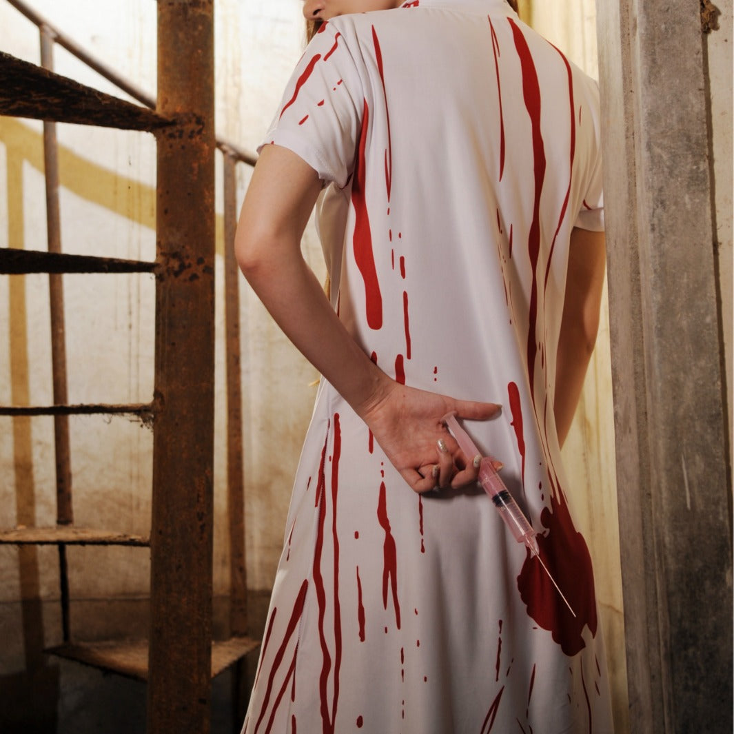 Person in a white dress with red bloodstains holding a syringe in a dimly lit room.