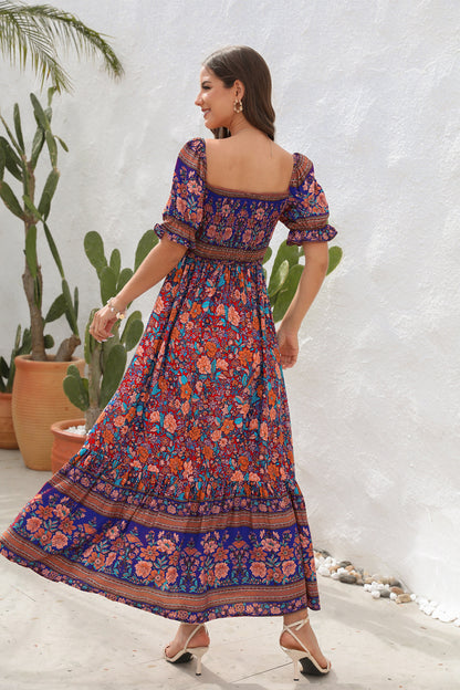 Woman wearing a floral dress standing against a white wall with plants.