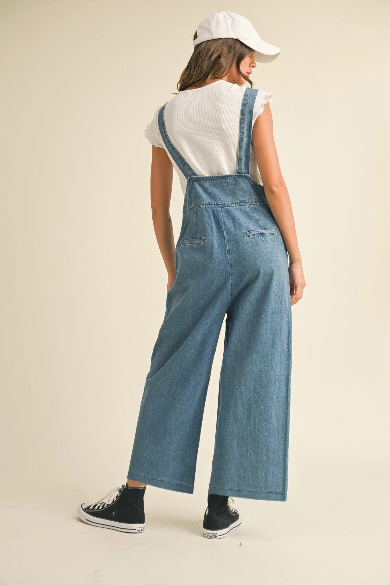 Person wearing a denim jumpsuit on a beige background Women retro loose straight denim suspender pants in washed blue