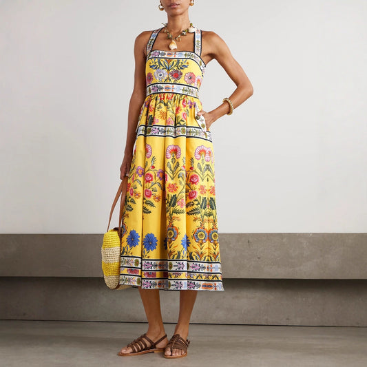 Woman wearing a yellow floral dress holding a straw bag against a neutral background