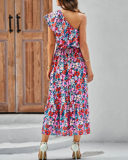 Woman wearing a colorful floral one-shoulder dress against a wooden door background