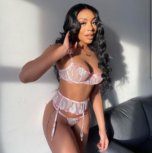 Woman wearing a pink lace lingerie set against a white wall.