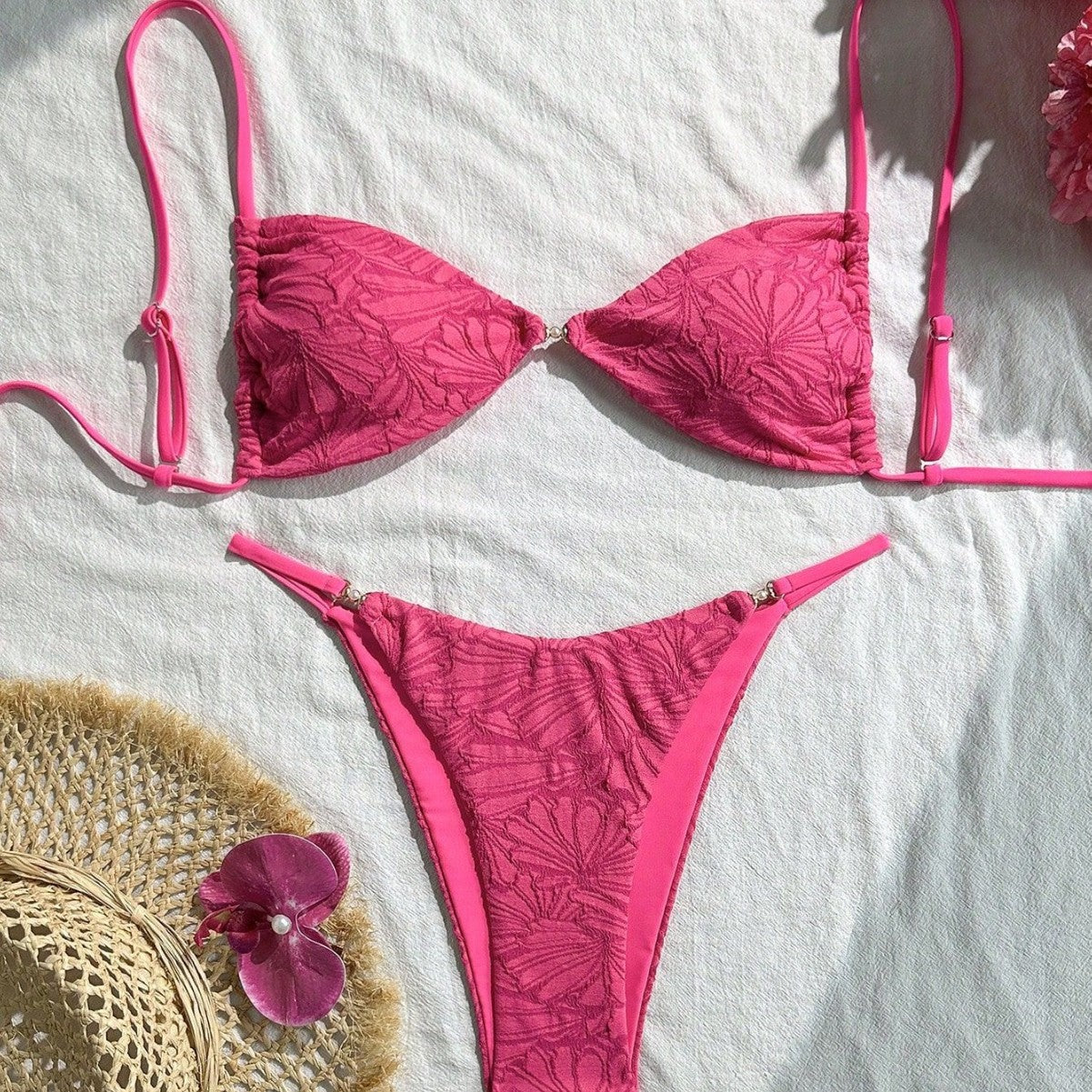 Pink bikini set on a white surface with a straw hat and pink flower.