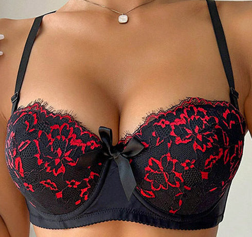 Person wearing a black lace bra with red floral patterns and denim shorts.