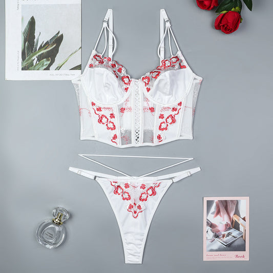 White lingerie set with red floral patterns on a gray surface with a perfume bottle and rose.