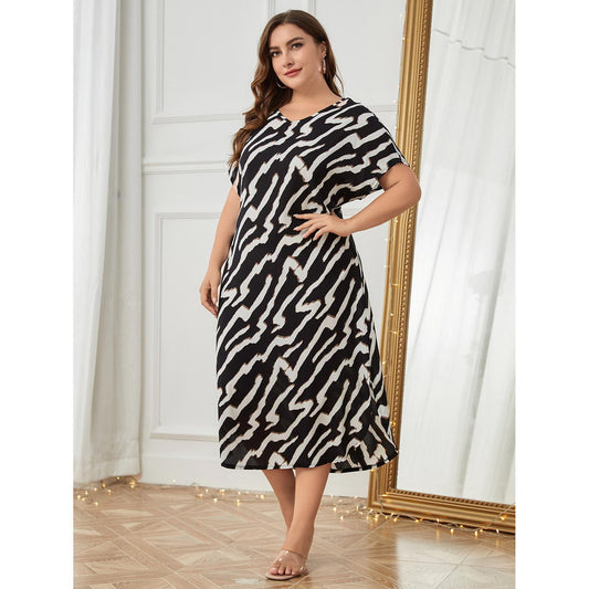 Woman wearing a black and white patterned dress in a room with white walls and a wooden floor.