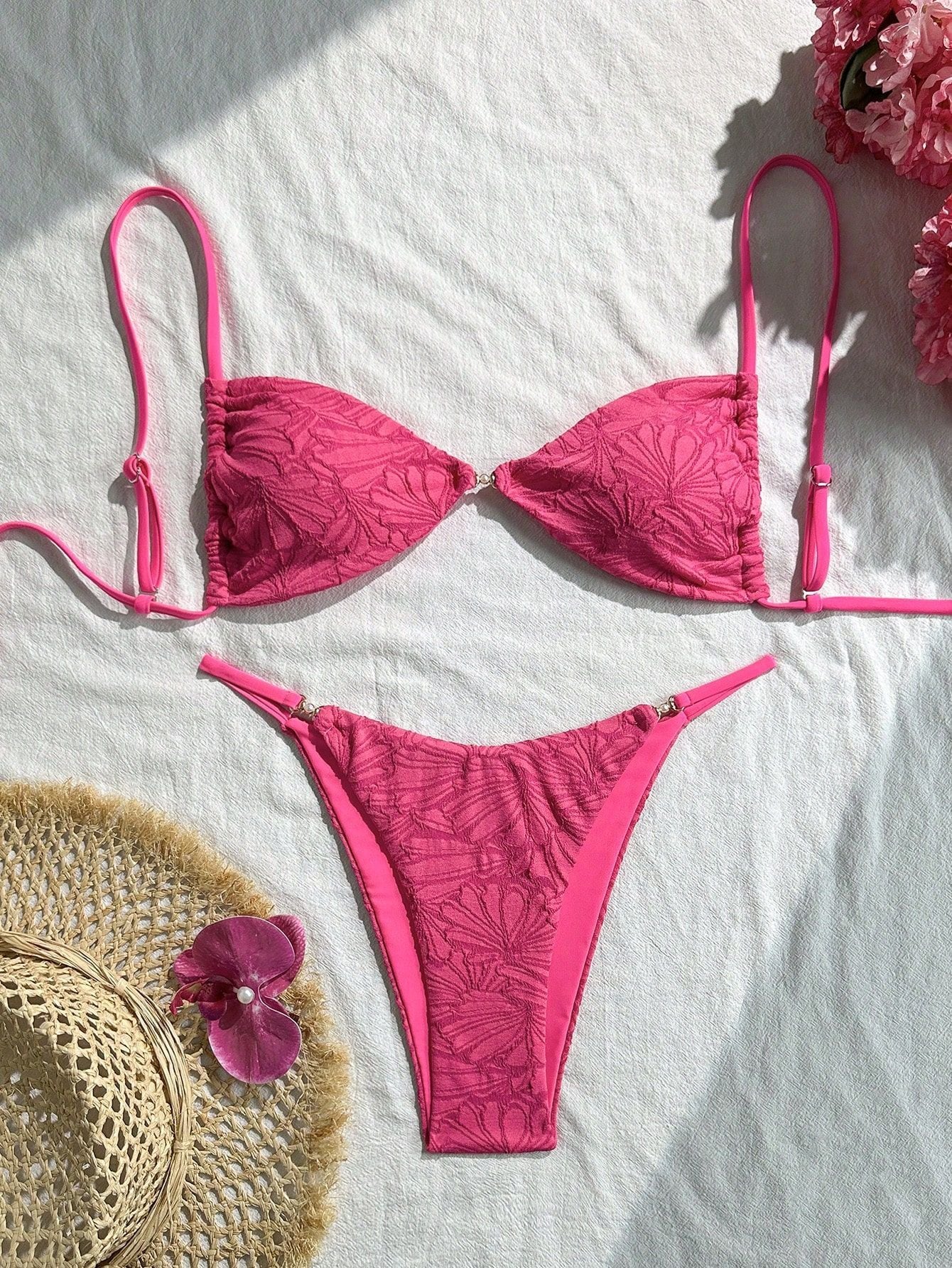 Pink bikini set on a white surface with a straw hat and flowers.