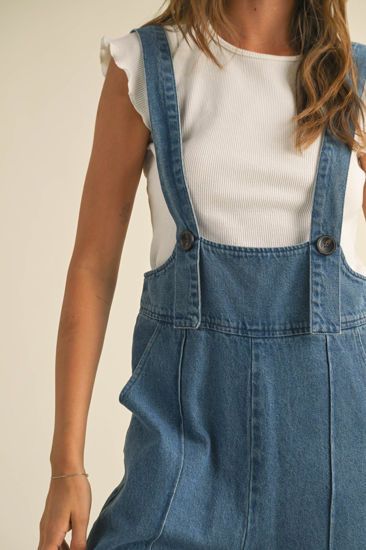 Person wearing a white top and blue denim overalls on a beige background Women retro loose straight denim suspender pants in washed blue
