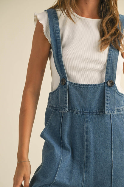 Person wearing a white top and blue denim overalls on a beige background Women retro loose straight denim suspender pants in washed blue
