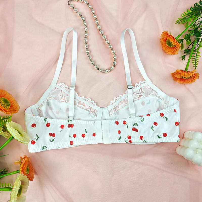 White lace bra with cherry pattern on a pink background with flowers and jewelry.
