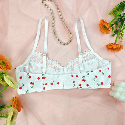 White lace bra with cherry pattern on a pink background with flowers and jewelry.