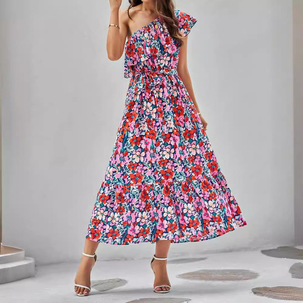 Woman wearing a colorful floral one-shoulder dress on a plain background