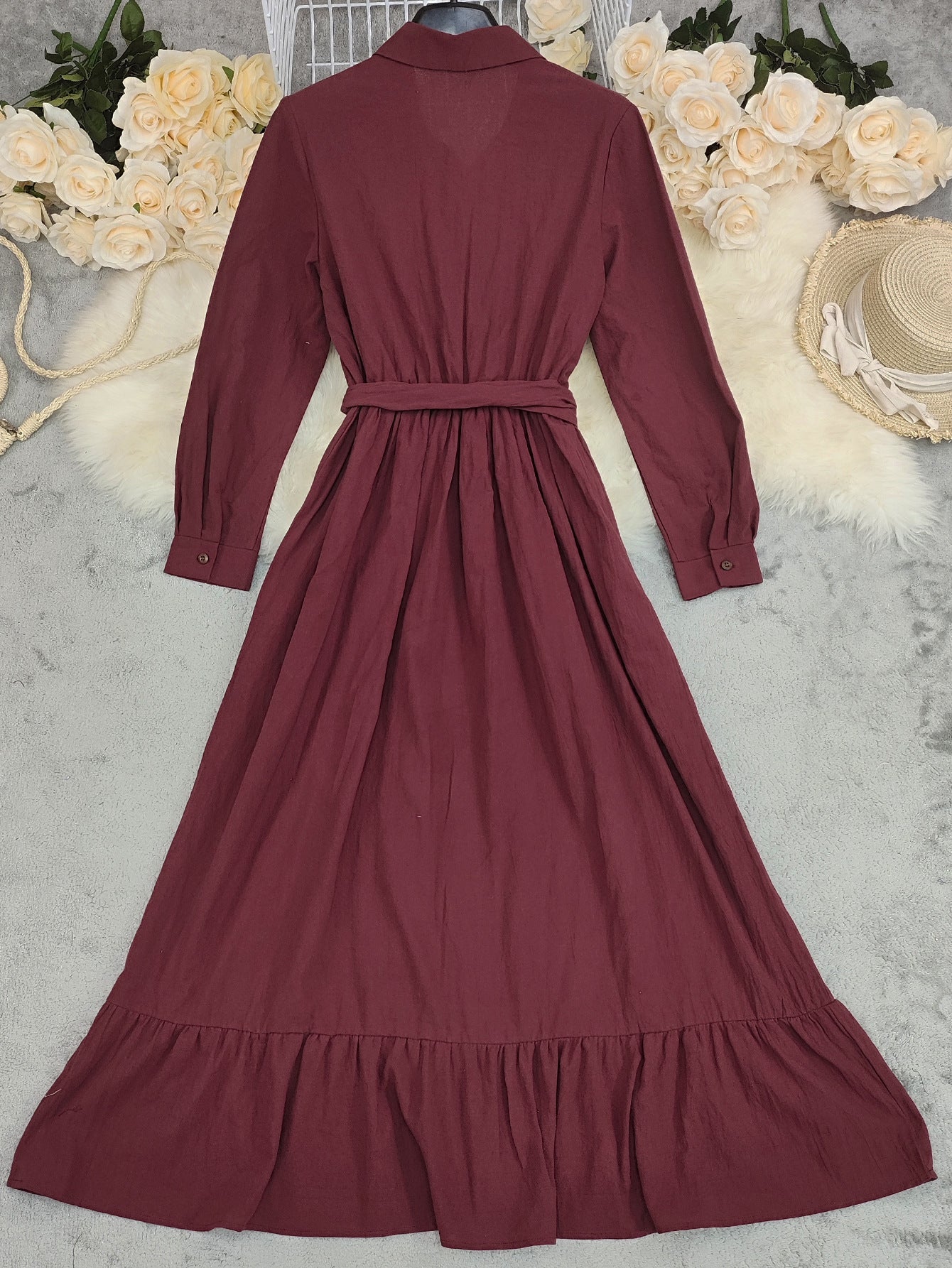 Maroon dress with long sleeves on a neutral background with flowers and a hat.