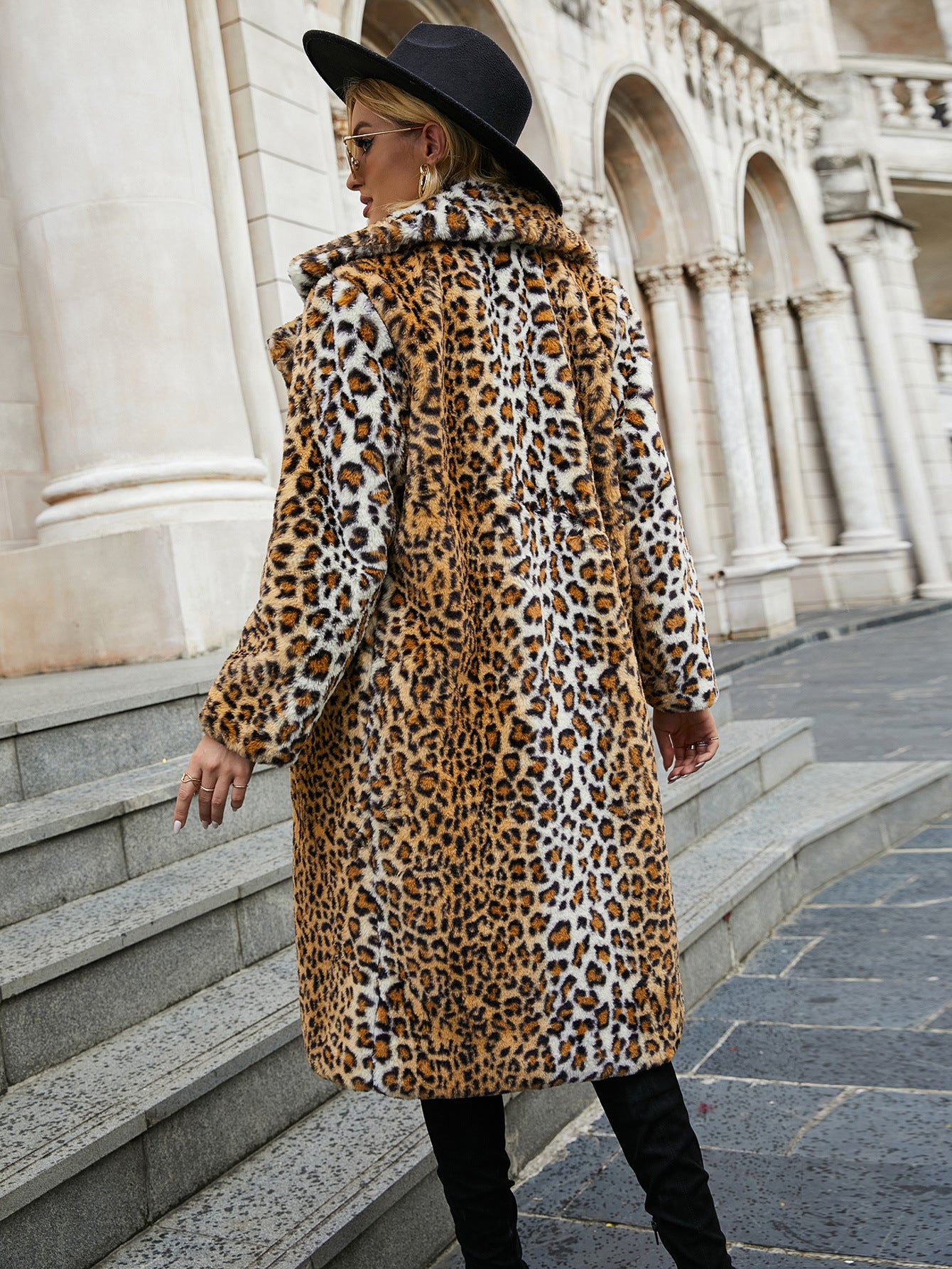 Person wearing a leopard print coat and black hat in an urban setting